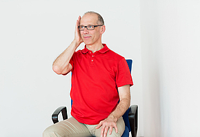 Ein Mann sitzt auf einem Stuhl. Er drückt seine Handfläche gegen die Wange.