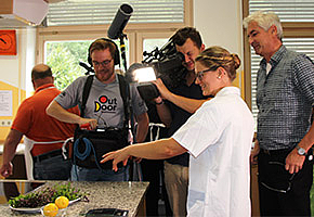 Diätassistentin zeigt einem Kamerateam eine zubereitete Speise.