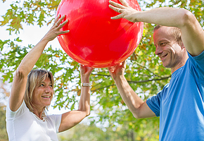 Eine Frau und ein Mann halten gemeinsam einen Gymnastikball in die Höhe.